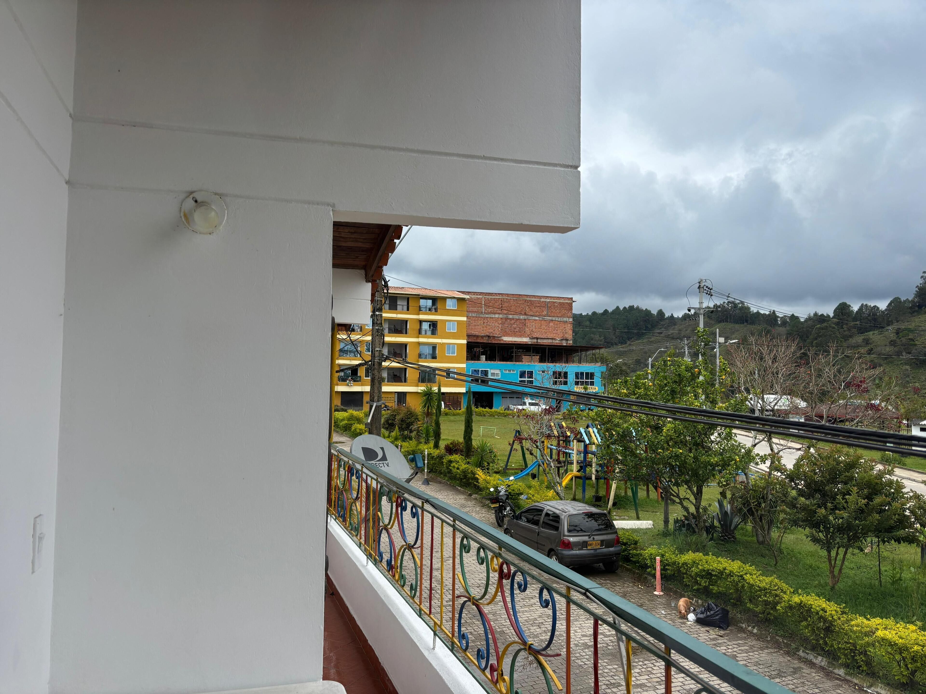 A balcony with a view of a playground, a parked car, and a building with multiple floors.