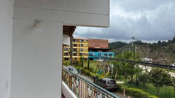 A balcony with a view of a playground, a parked car, and a building with multiple floors.