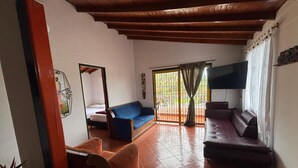 A living room with a sofa, a chair, a TV, and a balcony with a view. - Apartamento Zócalos de Guatape (Guatape)