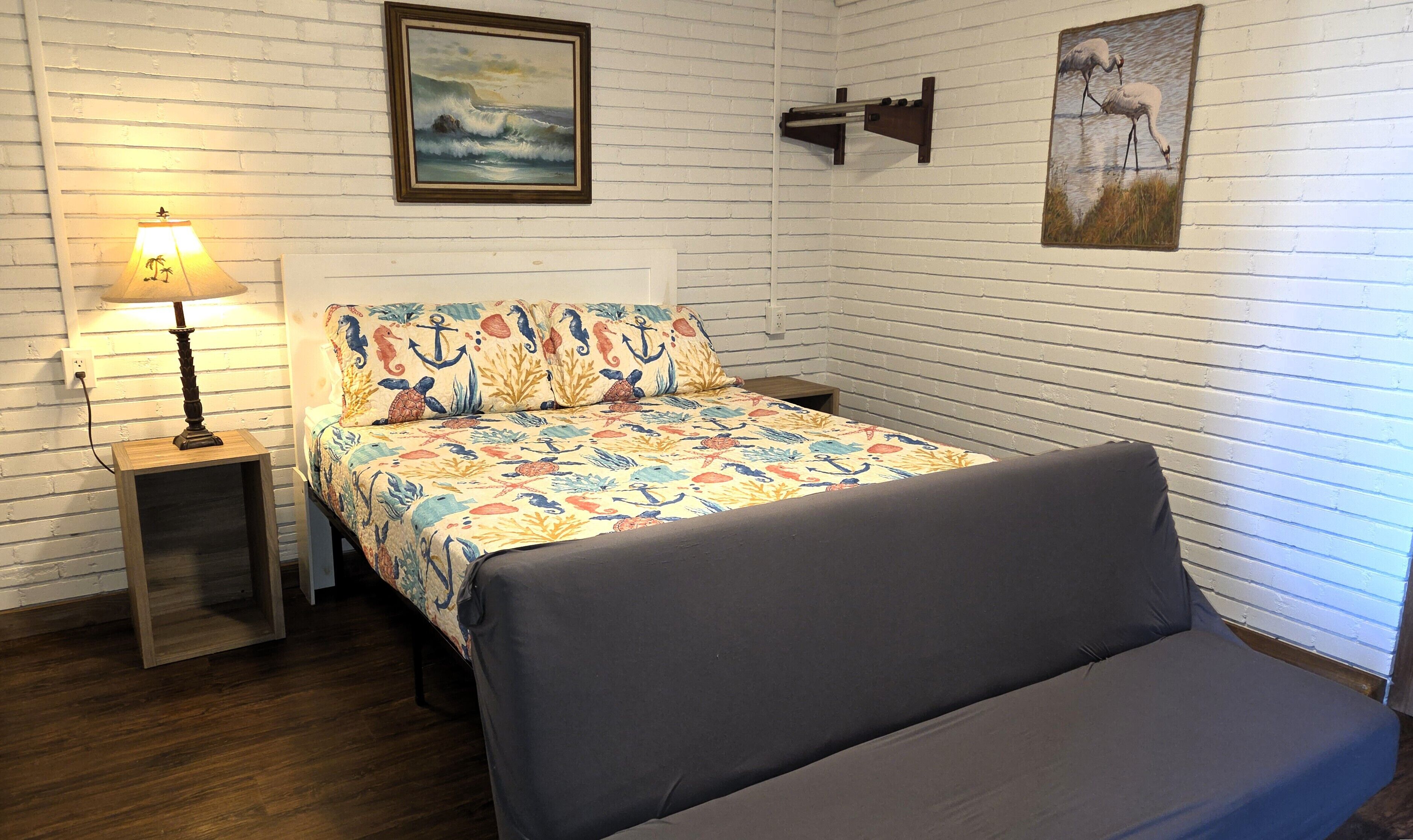 A room with a bed, a nightstand with a lamp, and two paintings on the wall.