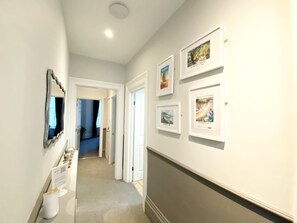 A hallway with framed pictures on the wall, a mirror, and a white door leading to another room. - Spacious, dog friendly, 2 bedroom family accommodation short distance from seafront and beaches. (Torquay)