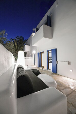 A modern outdoor seating area with white and black cushions, a stone floor, and a blue door. - Mykonos Townhouse Gem (Mykonos)