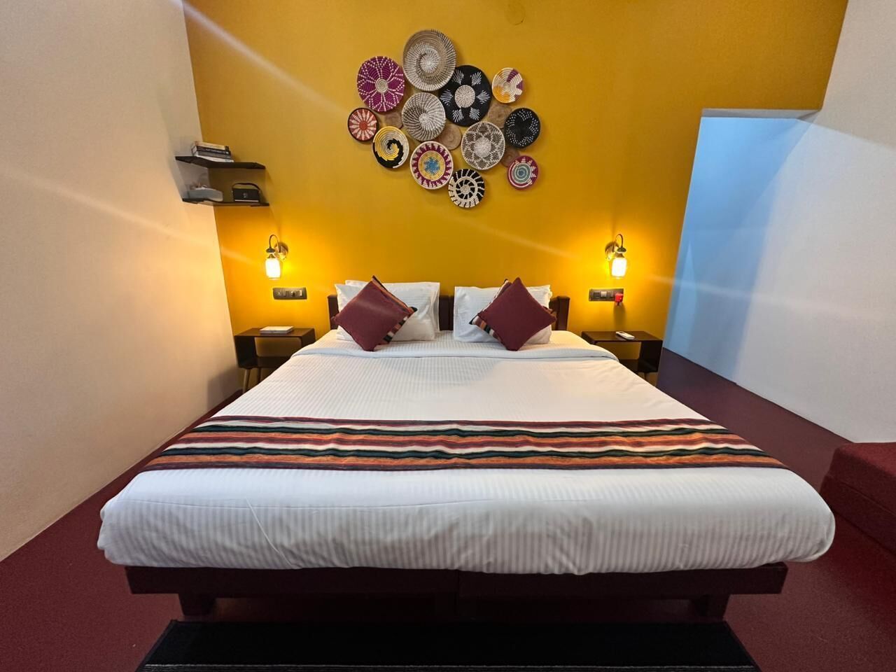 A hotel room with a bed, two bedside tables, a wall-mounted lamp, and a decorative wall hanging.