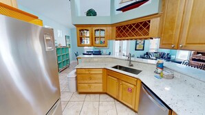 A modern kitchen with wooden cabinets, a stainless steel refrigerator, and a large island with a sink. - Mango Tango - Dog Friendly 5 BR home in gated community close to beach (Miramar Beach)