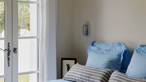 A bedroom with two beds, a large window with curtains, a bedside table, and a wall-mounted light fixture. - Villa Ortensa - à Hossegor - With swimming pool (Soorts-Hossegor)