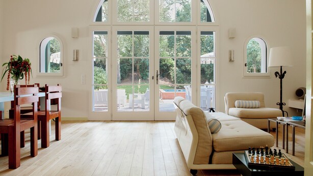A spacious living room with a large arched window, a beige sofa, a dining table with chairs, and a chessboard. - Villa Ortensa - à Hossegor - With swimming pool (Soorts-Hossegor)