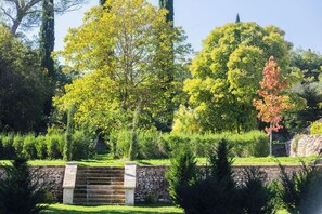 Una scala in pietra conduce a un muro di pietra, circondata da una vegetazione lussureggiante e alberi.