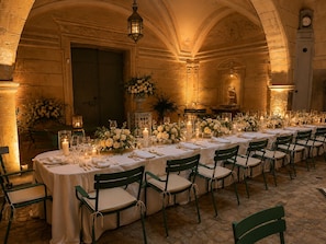 Una larga mesa dispuesta para un evento formal, con sillas, velas y arreglos florales.