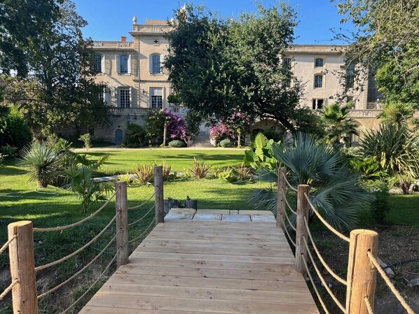 Un puente de madera que conduce a un edificio grande con un jardín delantero.