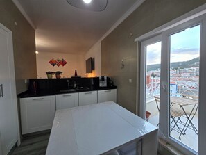 Eine kompakte Küche mit Essbereich, Blick auf die Stadt durch ein großes Fenster und einem kleinen Balkon mit Gartenmöbeln.