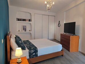 Ein ordentlich eingerichtetes Schlafzimmer mit Bett, Nachttischlampe, Kommode, Fernseher und Bücherregal.
