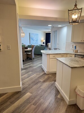 A modern kitchen with a marble countertop, wooden flooring, and white cabinetry. - Summer House 703A - Gulf Front (Orange Beach)