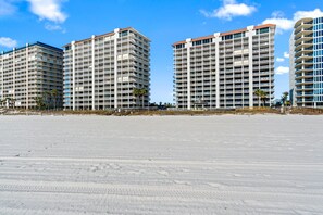 A beachfront hotel with multiple high-rise buildings, a sandy beach in the foreground, and palm trees. - Summer House 703A - Gulf Front (Orange Beach)