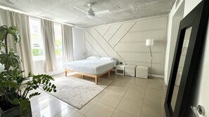 Ein modernes Schlafzimmer mit einem Bett, Nachttischen, einer Stehlampe und einem großen Fenster mit Vorhängen.