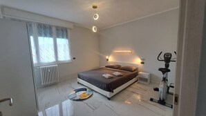 A modern bedroom with a bed, bedside lamps, a radiator, a window with curtains, a yoga mat, and a stationary exercise bike. - Casa Adelaide close to MM3 Family sized new apartment (Milano)
