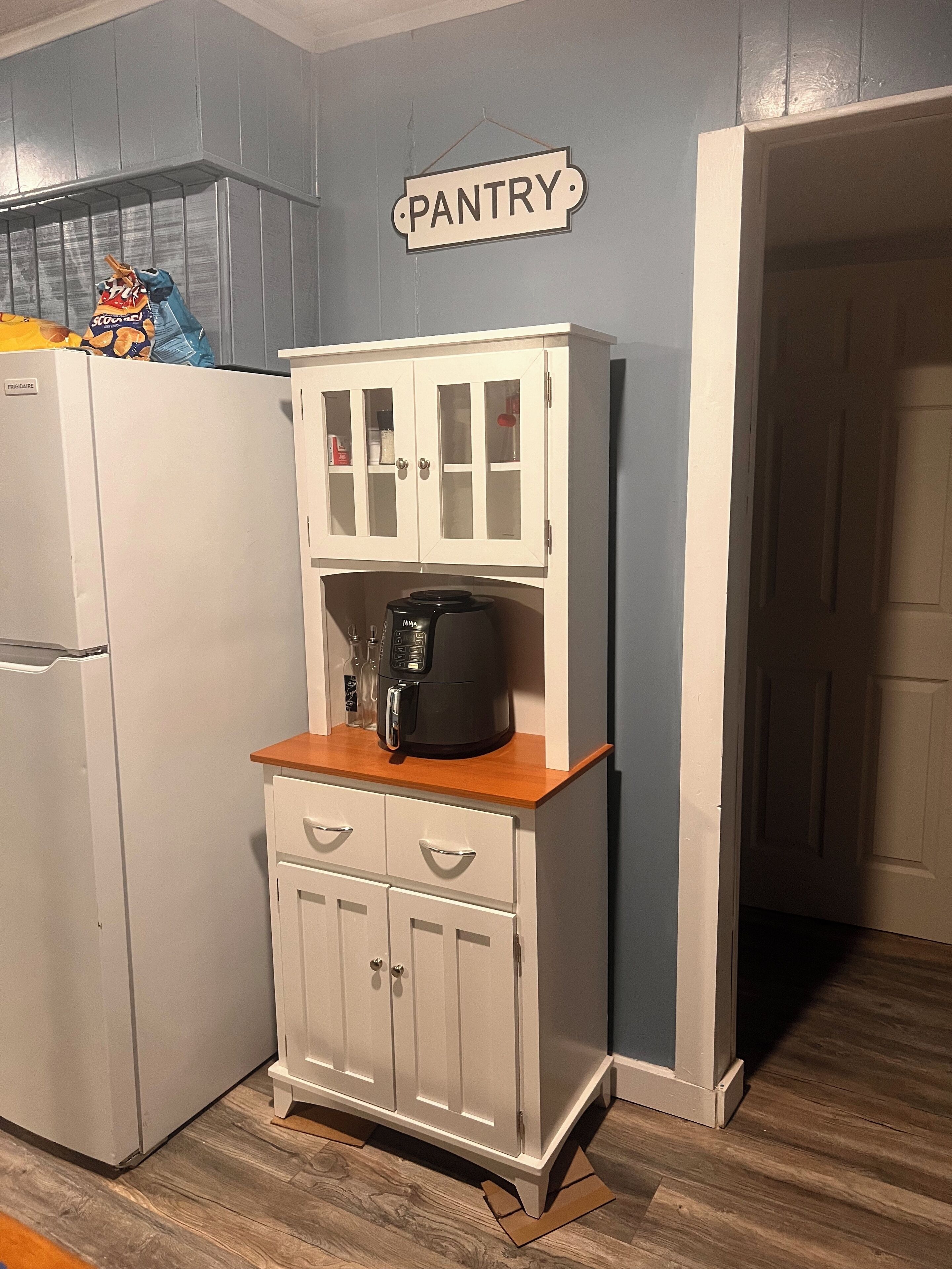A kitchen with a white cabinet labeled "PANTRY," a coffee maker, and a bag of snacks on the counter.