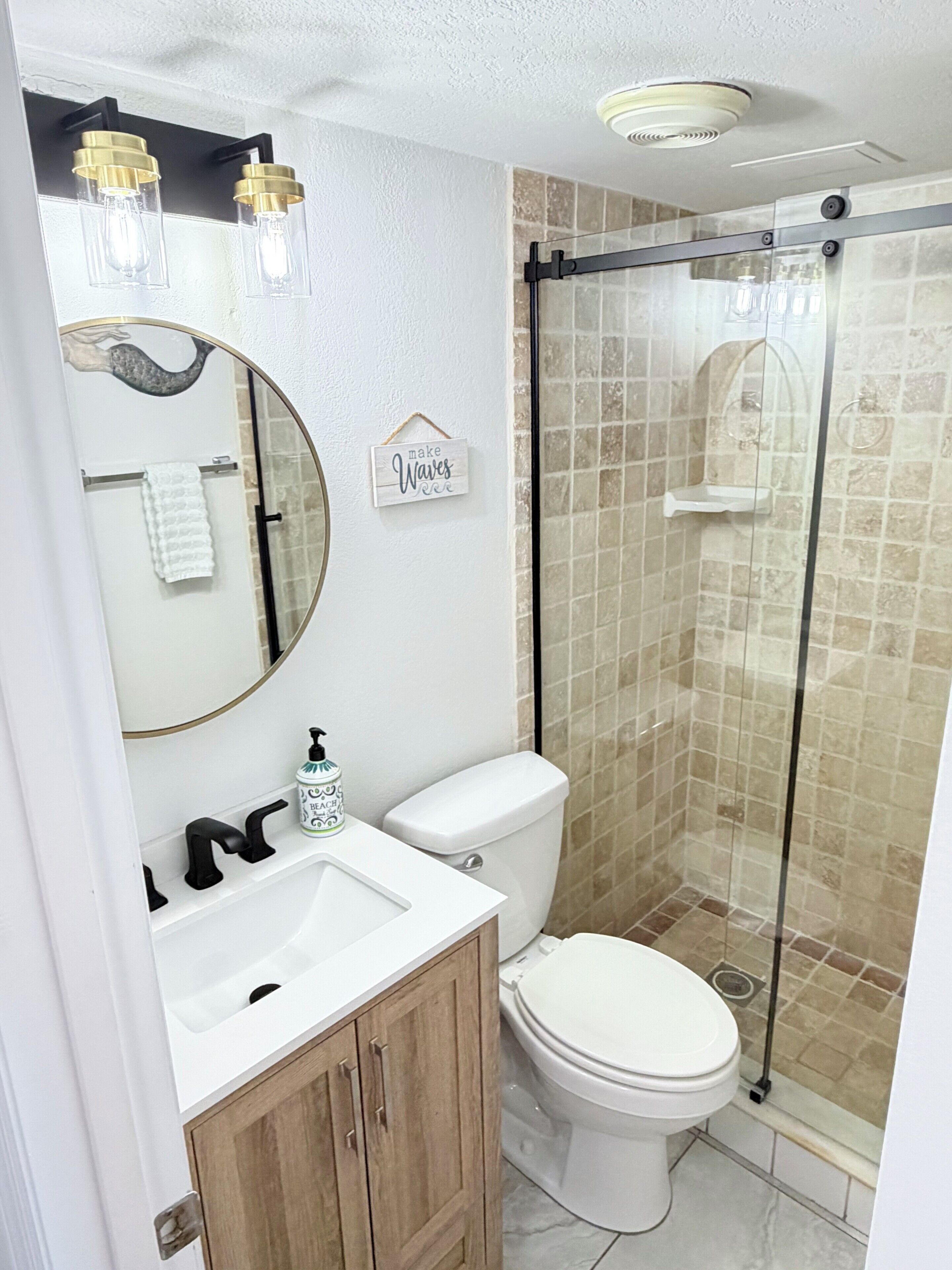 A bathroom with a toilet, sink, mirror, and shower.