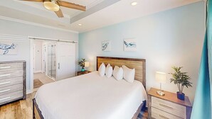 Een slaapkamer met een groot bed, een plafondventilator, een nachtkastje met lamp en kunst aan de muur.