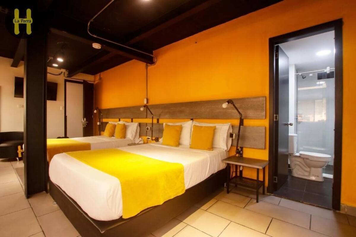 Une chambre d’hôtel avec deux lits, une tête de lit en bois, une petite table de chevet et une salle de bain visible à travers une porte ouverte.