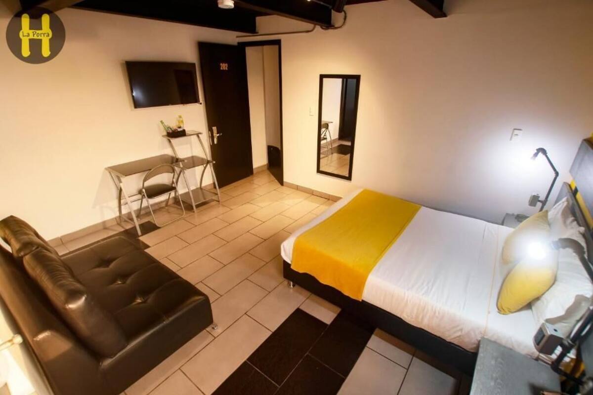 Une chambre d’hôtel équipée d’un lit, d’un bureau, d’une chaise, d’un canapé, d’une télévision et d’un miroir.