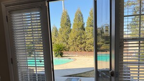Una stanza con una porta scorrevole in vetro che dà su un patio con piscina, un piccolo tavolo e vista su alberi alti.