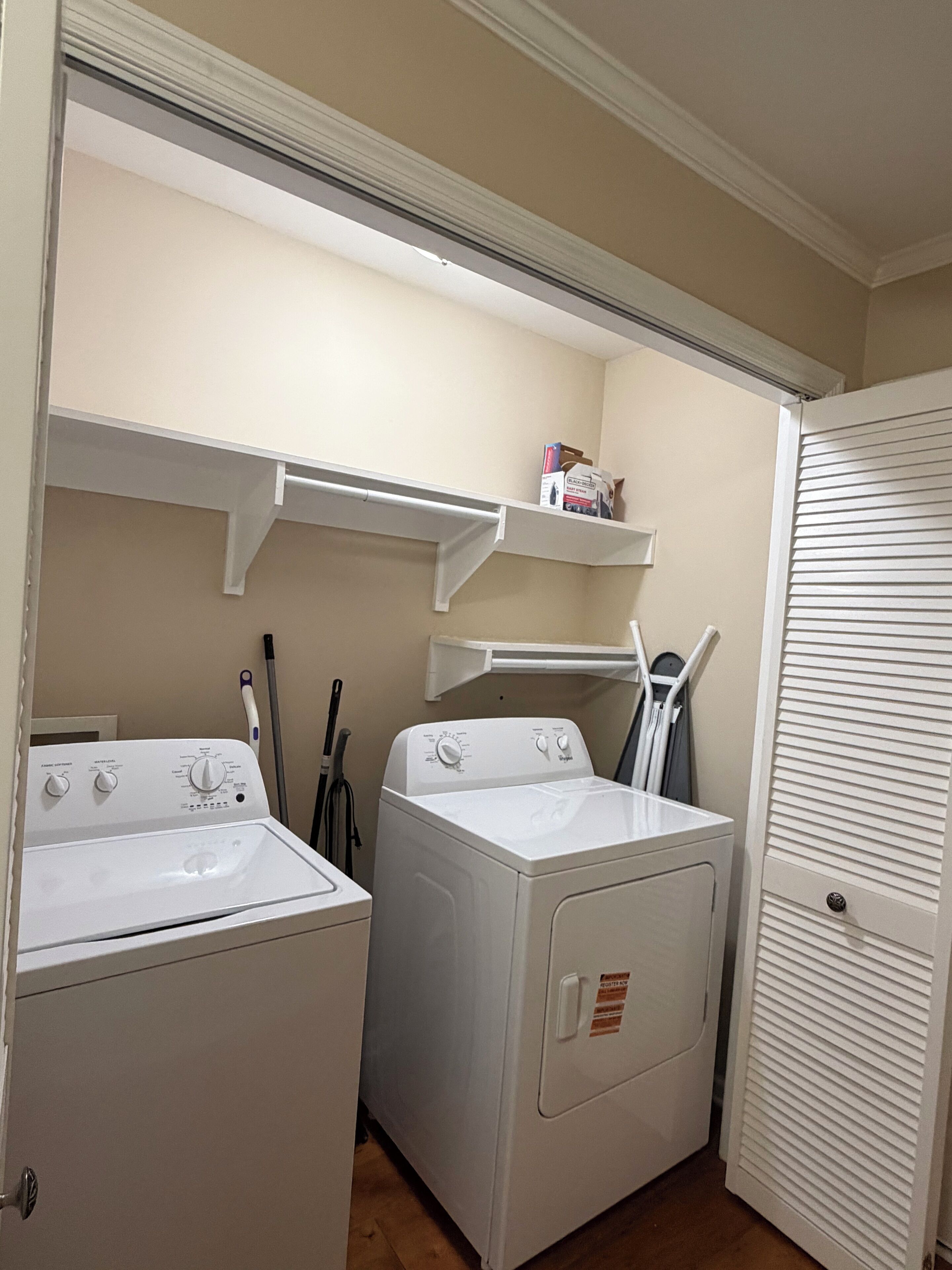 Un cuarto de lavandería con dos lavadoras, un tendedero y un estante con productos de limpieza.