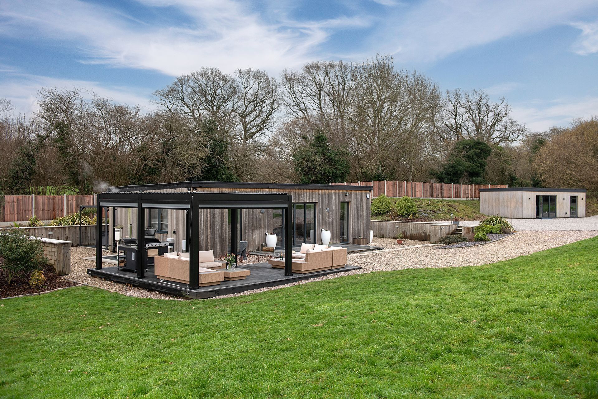 Un patio extérieur moderne, doté d’une véranda en verre, de mobilier d’extérieur et d’un espace barbecue.