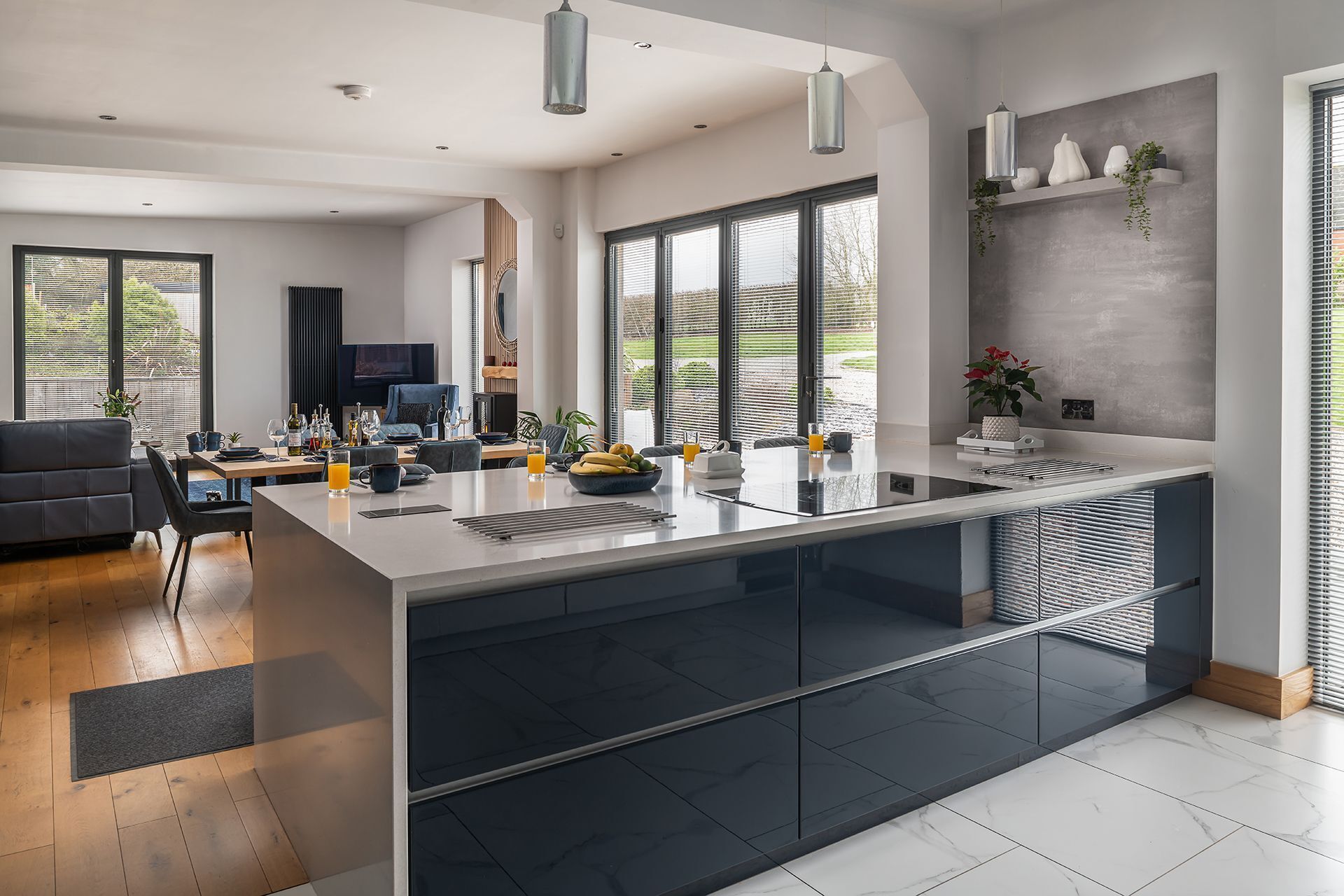 A modern kitchen with a central island, large windows, and a dining area with a sofa and table.