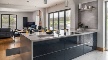 A modern kitchen with a central island, large windows, and a dining area with a sofa and table.
