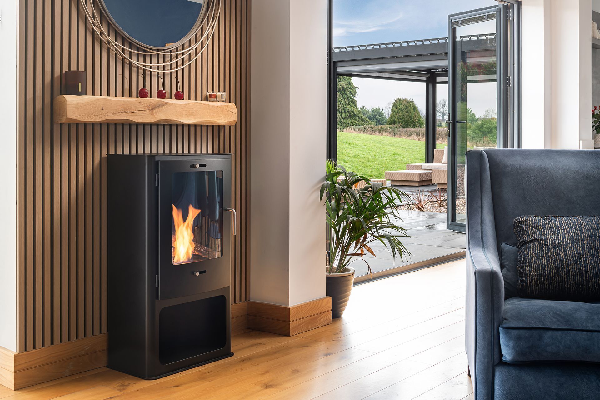 A modern living room with a wood-burning stove, a large window, and a view of the outdoors.