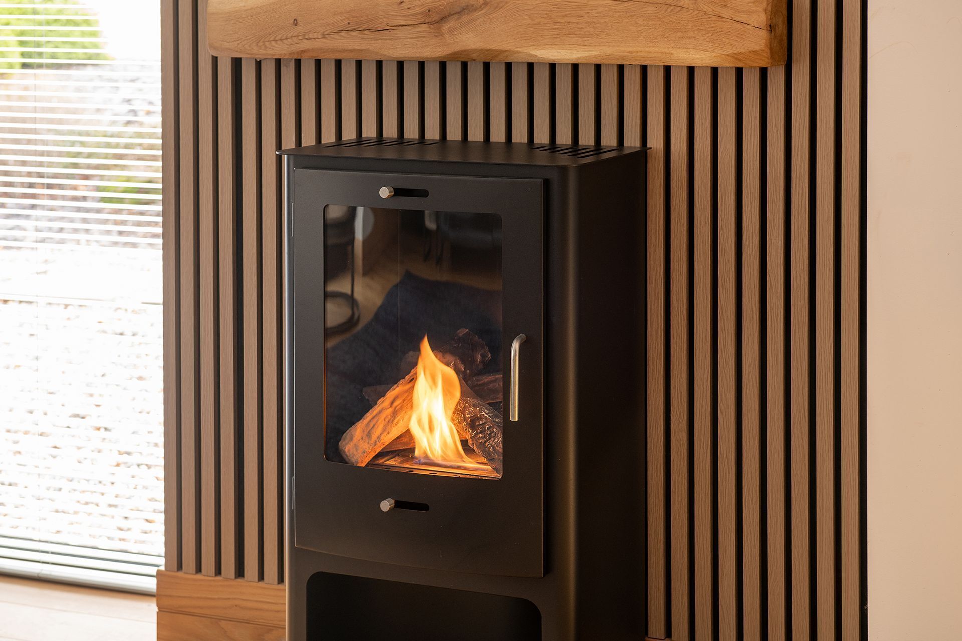 A modern wood-burning stove with a glass front, set against a wooden wall with vertical slats.
