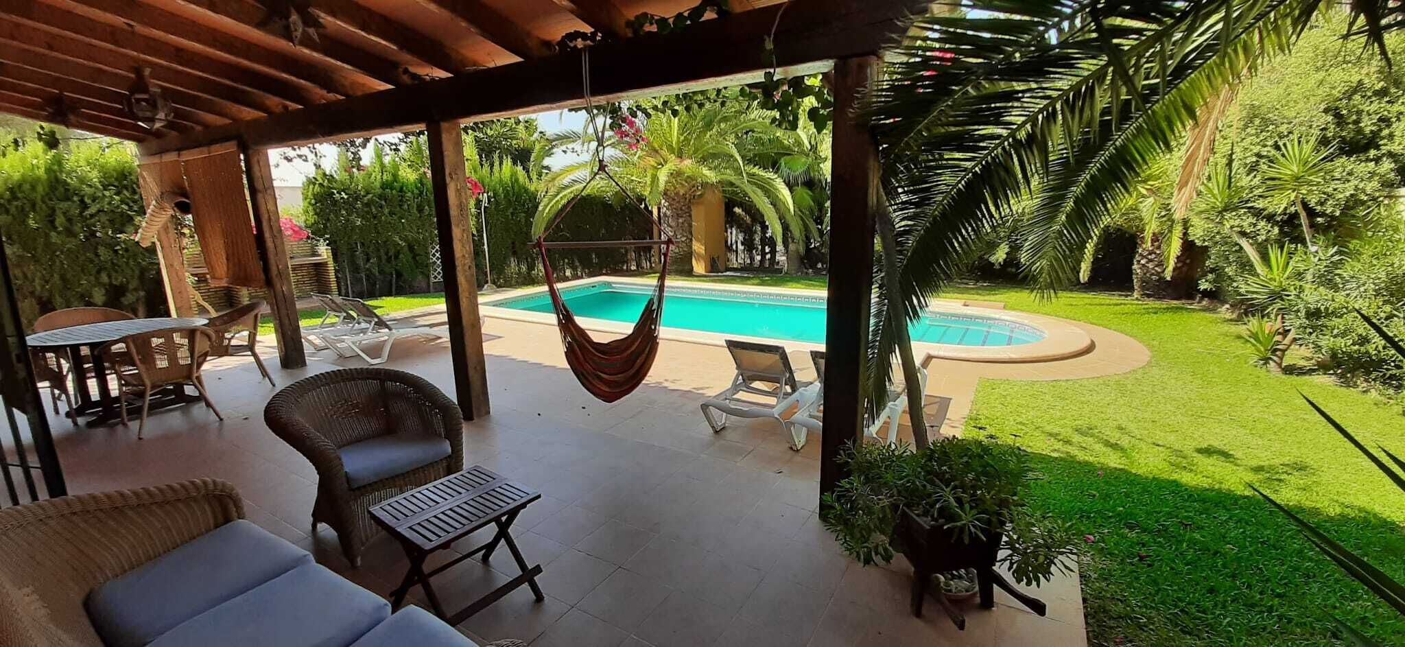 A covered outdoor area with a pool, lounge chairs, and a hanging hammock.