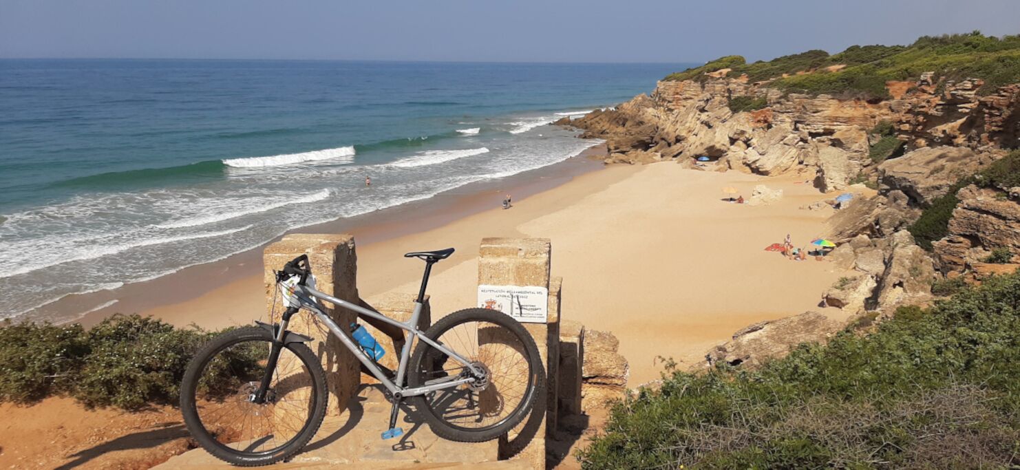 Une plage avec un vélo garé sur un rocher, un panneau et une falaise rocheuse.