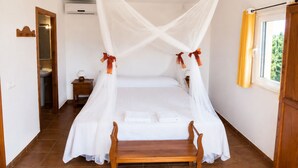 Une chambre à coucher avec un lit à baldaquin, un banc en bois, une table de chevet et une fenêtre avec des rideaux.