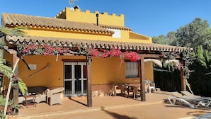 Un bâtiment jaune avec un toit en tuiles, un patio couvert avec des chaises et des tables, et une enseigne sur laquelle on peut lire « La Flor ».