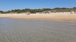 A beach with clear shallow waters, a sandy shore, and a few people and umbrellas in the distance. - Pool villa (6p) with private pool in subtropical garden (Conil de la Frontera)