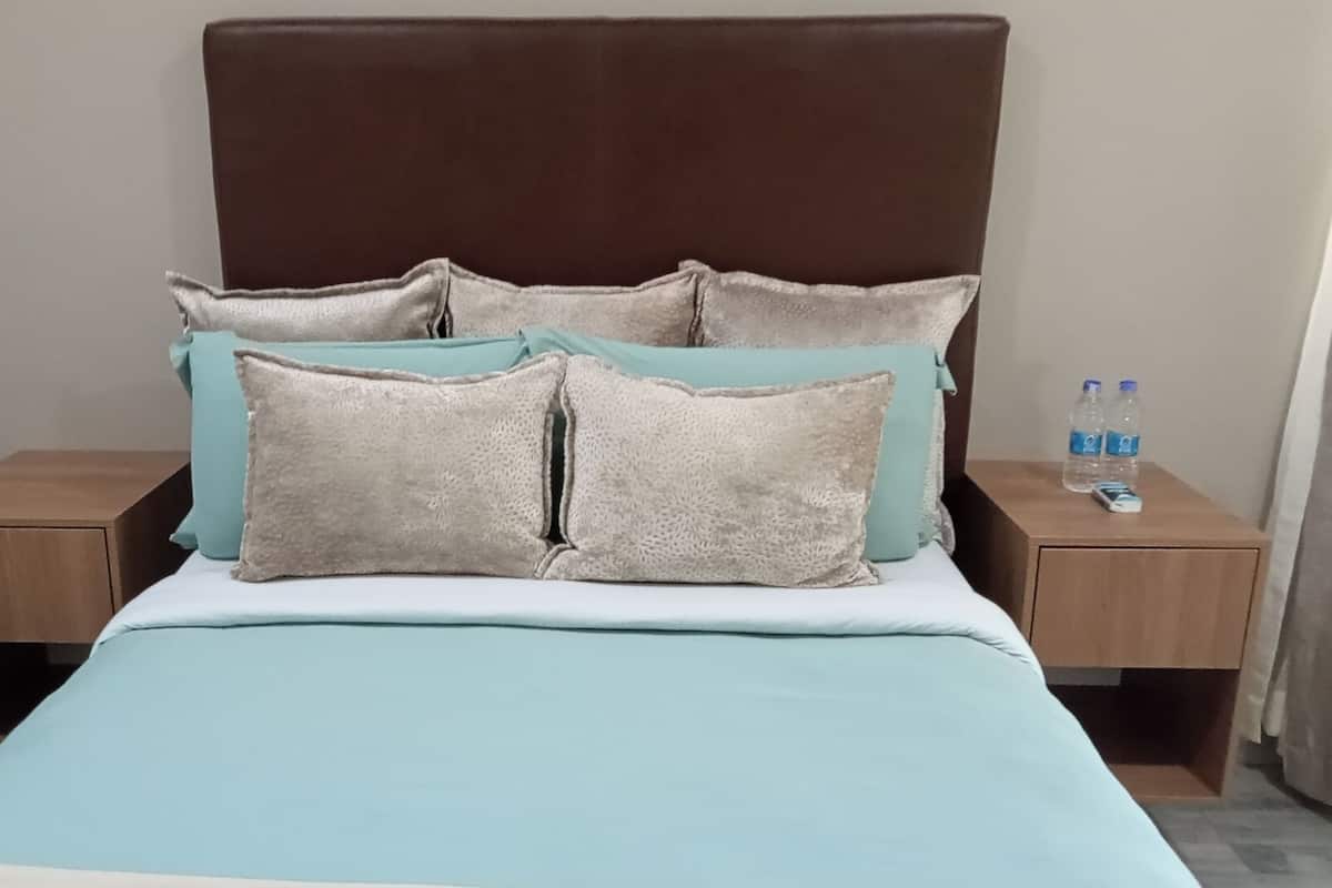 A neatly made bed with light blue bedding and four pillows, two of which are beige. There are two wooden nightstands on either side of the bed, each with a water bottle on top.