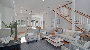 A spacious living room with a staircase, a kitchen in the background, and a dining area. - New Listing!  -Satilla Cottage -Coast Cottages (St Simons Island)