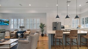 A spacious kitchen with white cabinets, a central island with bar stools, and pendant lighting. - New Listing!  -Satilla Cottage -Coast Cottages (St Simons Island)