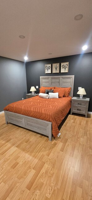 Un dormitorio con cama, dos mesitas de noche, cabecero y suelo de madera.