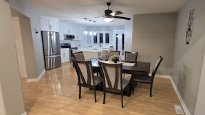A modern kitchen with stainless steel appliances, a dining area with a dark wood table and chairs, and a ceiling fan.