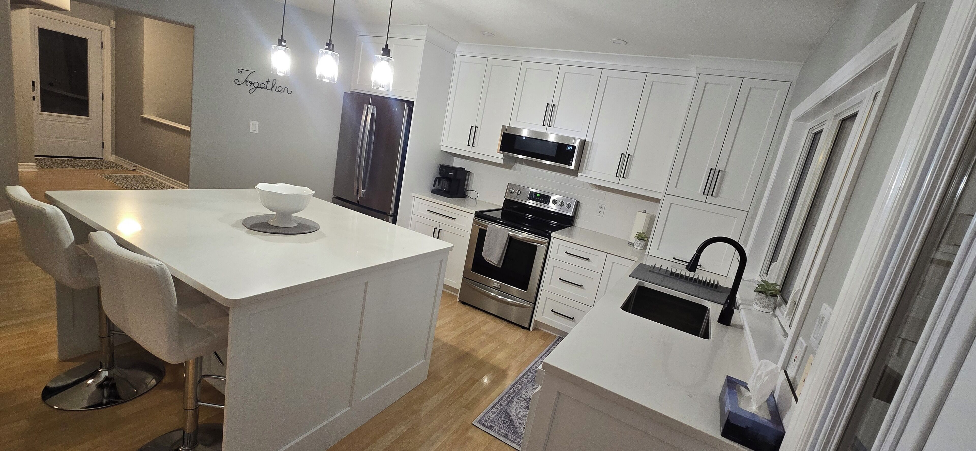 Une cuisine moderne avec des meubles blancs, des appareils en acier inoxydable et des luminaires suspendus.