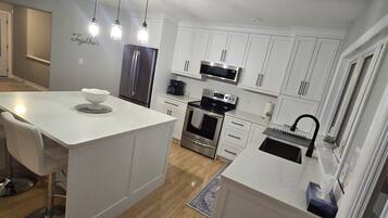 Une cuisine moderne avec des meubles blancs, des appareils en acier inoxydable et des luminaires suspendus.
