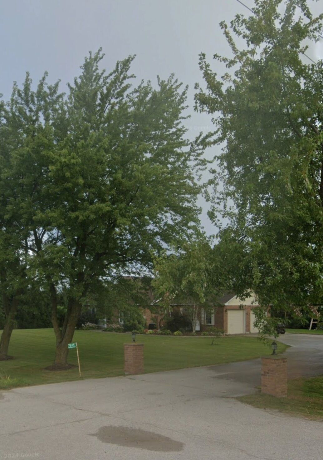 A residential driveway with a garage, surrounded by trees and a lawn.
