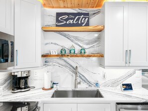 A kitchen with white cabinets, a marble backsplash, a coffee maker, and a sign that reads 'Stayty.' - Perfect Beach Escape - Charming 1 Bedroom Condo Just Steps From The Sand (Bradenton Beach)