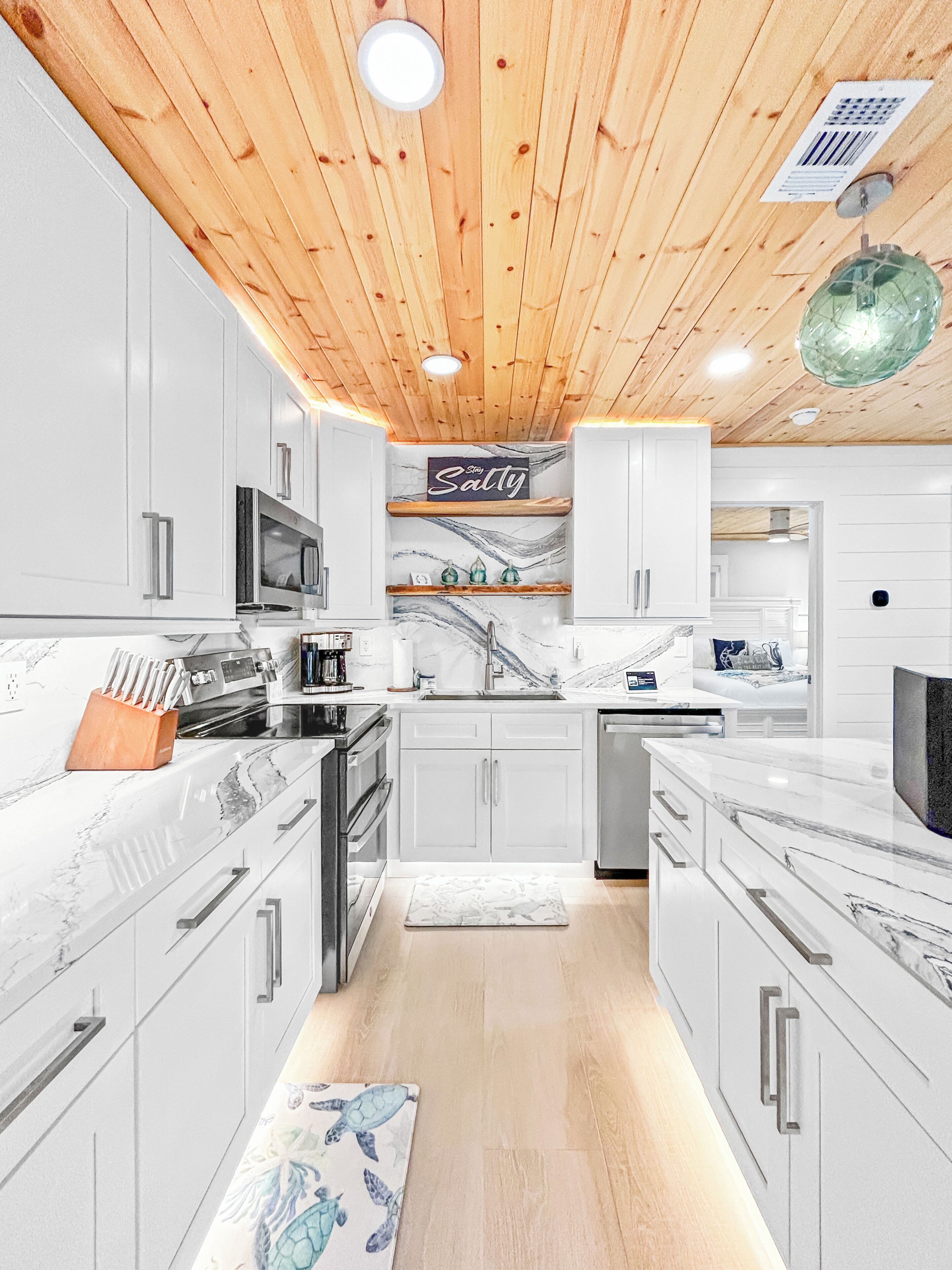 A modern kitchen with white cabinets, a wooden ceiling, and a marble countertop.