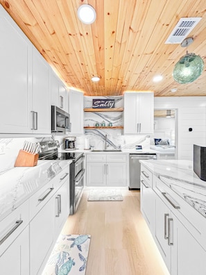 A modern kitchen with white cabinets, a wooden ceiling, and a marble countertop. - Perfect Beach Escape - Charming 1 Bedroom Condo Just Steps From The Sand (Bradenton Beach)
