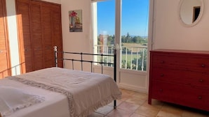 A bedroom with a bed, a dresser, a balcony with a view, and a window.