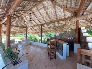 A covered outdoor area with a thatched roof, seating arrangements, and a stone wall with a bar counter. - Modern Tropical, no 21, Cabarete Studio: Pools & BBQ (Cabarete)