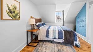Une chambre à coucher avec un lit, une table de chevet, une lampe et une œuvre d’art.
